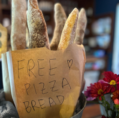 A container holding several pieces of bread with a sign that reads "FREE PIZZA BREAD" in handwritten letters.