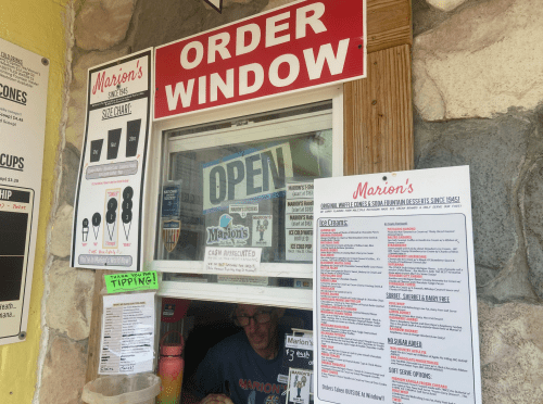 A small order window at Marion's, featuring a menu and a sign that says "Open," with a person inside taking orders.