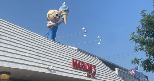 A quaint ice cream shop with a large ice cream cone mascot, featuring outdoor seating and families enjoying treats.
