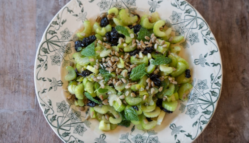 A plate of celery salad topped with sunflower seeds, dried fruits, and fresh mint on a decorative dish.