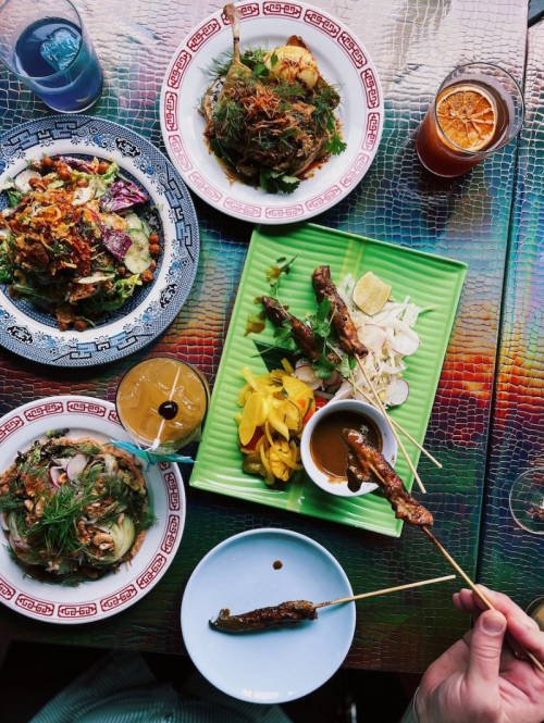 A vibrant spread of dishes including salads, skewers, and drinks on a colorful table.