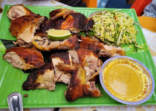 A platter of roasted chicken pieces with lime, a side of coleslaw, and a small bowl of sauce on a green tray.