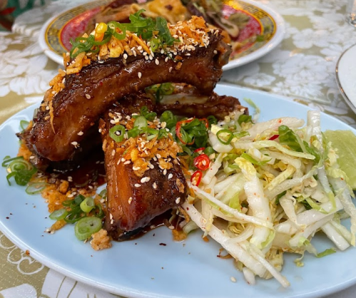 A plate of glazed ribs topped with sesame seeds and green onions, served with a side of shredded cabbage salad.