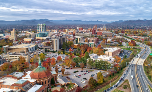 Aerial view of a city skyline with mountains in the background, showcasing autumn foliage and urban buildings.