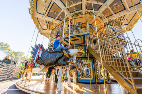 A child rides a carousel featuring a large eagle, with other children and the carousel structure in the background.