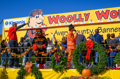 A colorful parade float with a large "Woolly Worm" sign, featuring a mascot and people celebrating in autumn attire.