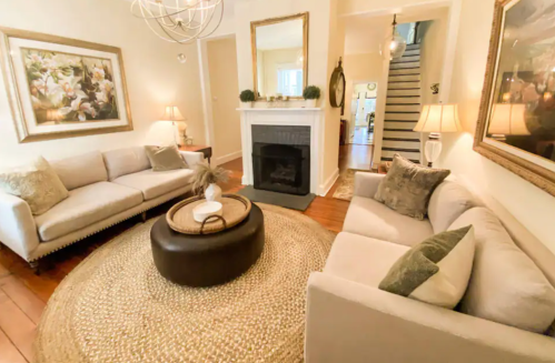 Cozy living room with two sofas, a round coffee table, and a fireplace, featuring warm lighting and decorative art.