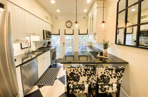 Modern kitchen with black and white decor, stainless steel appliances, and a stylish dining area featuring cow-print chairs.