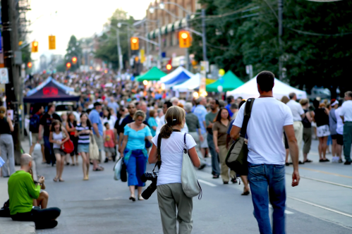 A busy street filled with people walking, food stalls, and colorful tents during a lively outdoor event.