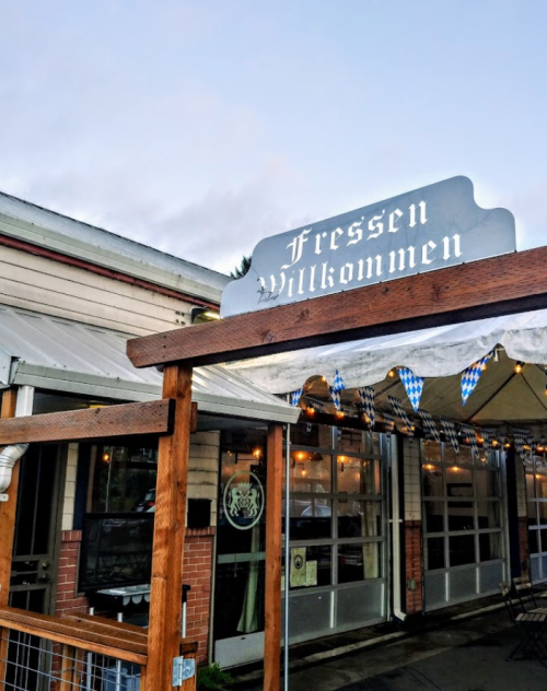 Sign reading "Fressen Willkommen" outside a restaurant with a wooden structure and festive decorations.