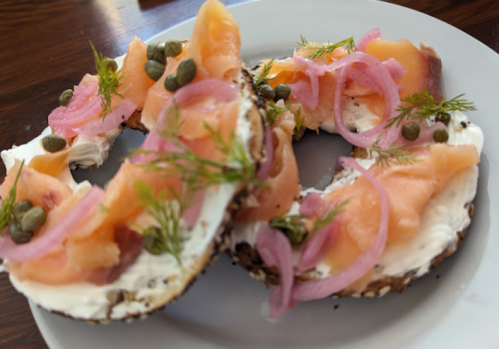 A plate with bagels topped with cream cheese, smoked salmon, capers, pickled onions, and fresh dill.