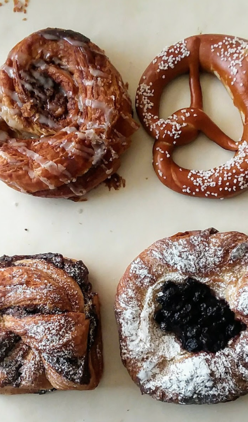 A variety of baked goods including a cinnamon roll, a pretzel, and pastries with powdered sugar and fruit filling.