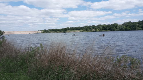 A serene lake scene with two kayakers paddling, surrounded by lush greenery and a cloudy sky.