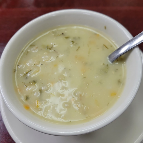A bowl of creamy soup with herbs, served with a spoon, on a white plate.