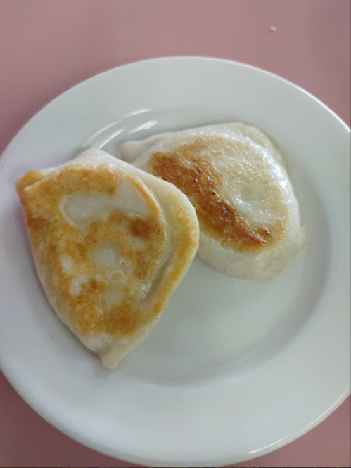 Two golden-brown dumplings on a white plate, with a slightly crispy exterior and soft interior.