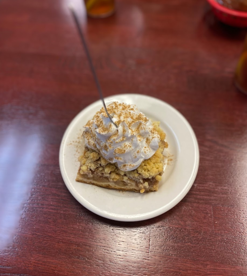 A slice of dessert topped with whipped cream and crumbled topping, served on a small white plate.