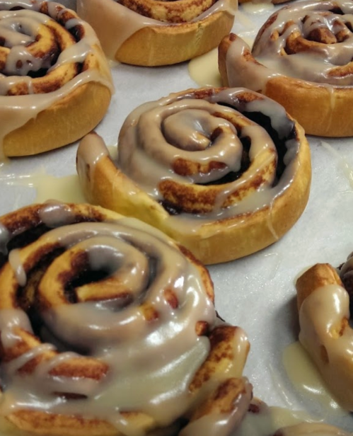 Freshly baked cinnamon rolls drizzled with creamy icing, arranged on parchment paper.