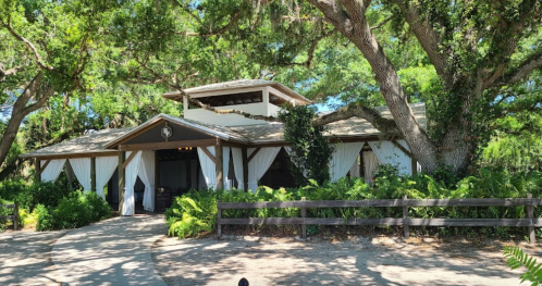 A charming building surrounded by trees and greenery, featuring a covered porch with white drapes.