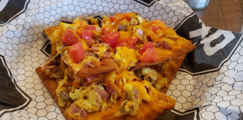 A plate of nachos topped with cheese, diced tomatoes, and a mix of meats on a paper-lined tray.