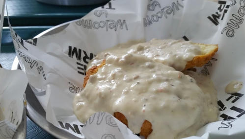 A plate of biscuits smothered in creamy sausage gravy, served in a basket lined with paper.