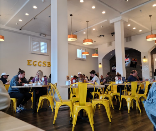 A busy restaurant interior with yellow chairs, patrons dining, and a warm, inviting atmosphere.