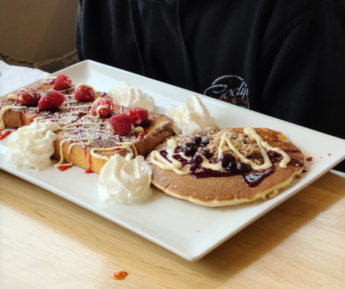 A plate of pancakes and French toast topped with whipped cream, berries, and drizzled sauces.