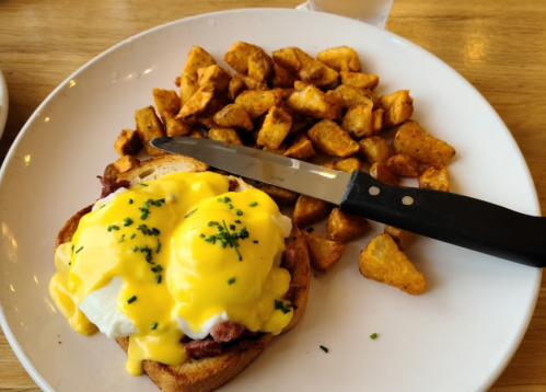 A plate of eggs Benedict with poached eggs and hollandaise sauce on toast, served with seasoned potato cubes.