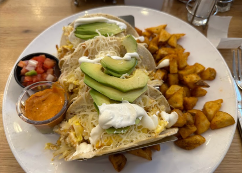 Two breakfast tacos with eggs, avocado, cheese, and sour cream, served with seasoned potatoes and salsa on the side.