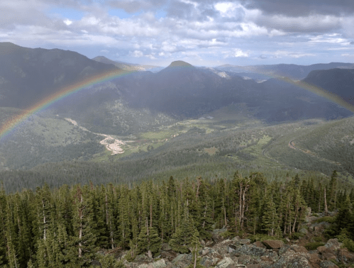 A scenic mountain view with lush green valleys and a double rainbow arching across the sky after a rain.