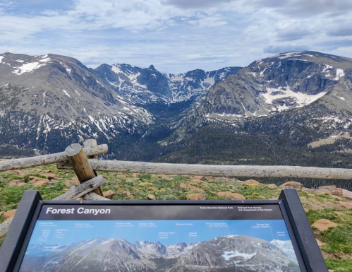 View of Forest Canyon with a sign in the foreground, showcasing mountains and a cloudy sky in the background.