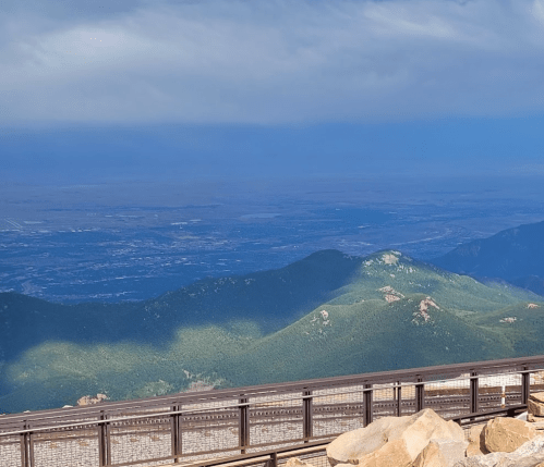 A panoramic view of green mountains under a cloudy sky, with a valley stretching into the distance.