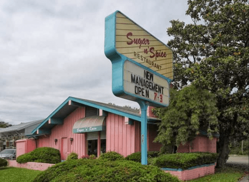 A pink restaurant building with a sign reading "Sugar n' Spice" and "New Management Open 7-3" under a cloudy sky.