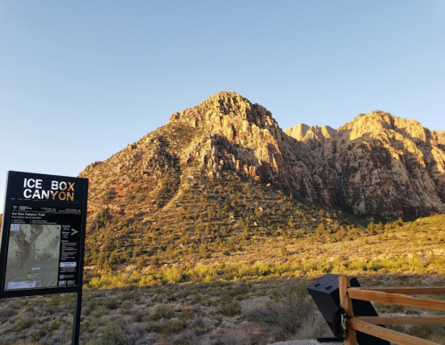 Sign for Ice Box Canyon Trail with rocky mountains in the background under a clear sky.
