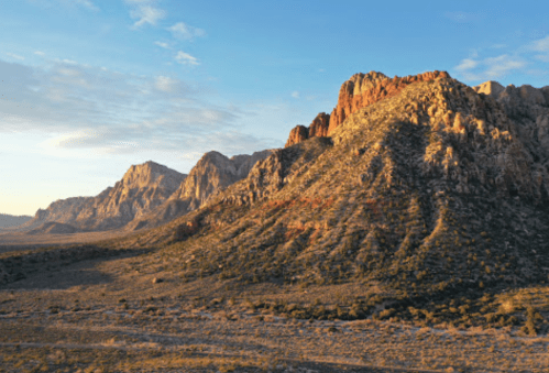 A scenic view of rugged mountains under a clear sky, with sunlight illuminating the rocky terrain.