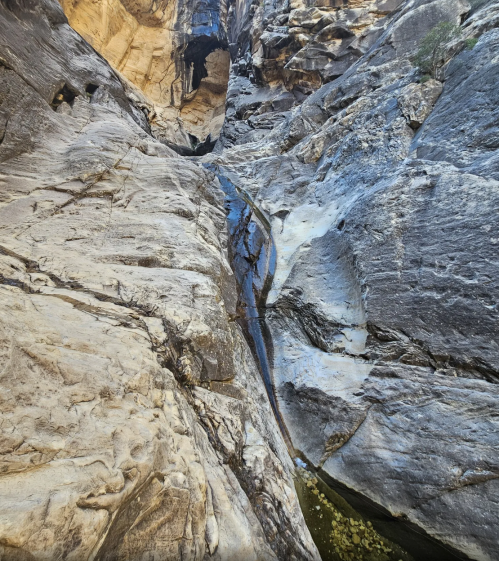 A narrow canyon with smooth, rocky walls and a small stream of water flowing through the center.