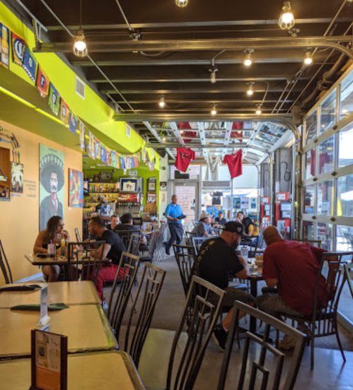A vibrant restaurant interior with colorful decor, patrons dining, and a staff member serving in a spacious setting.