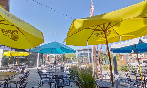 Outdoor dining area with colorful umbrellas, tables, and a clear blue sky in a lively urban setting.