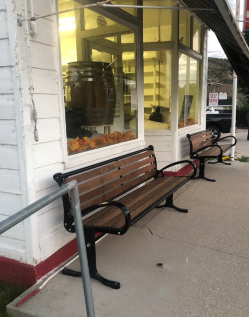Two wooden benches with black metal frames are positioned outside a shop with large windows and autumn decorations.