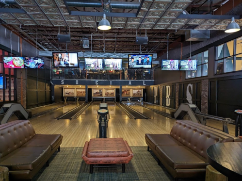 A modern bowling alley with multiple lanes, seating areas, and large screens displaying sports.