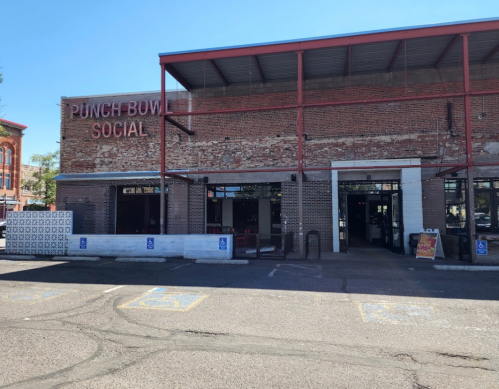 Exterior of Punch Bowl Social, a brick building with large windows and a sign, set in a sunny urban environment.