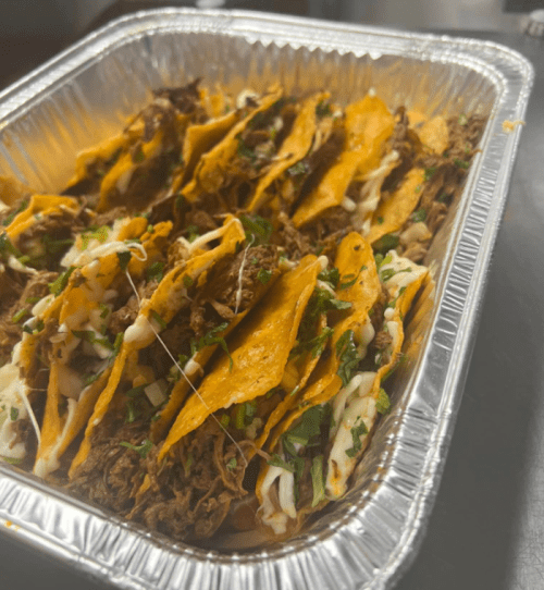 A tray of stacked tacos filled with shredded meat, topped with herbs and sauces.