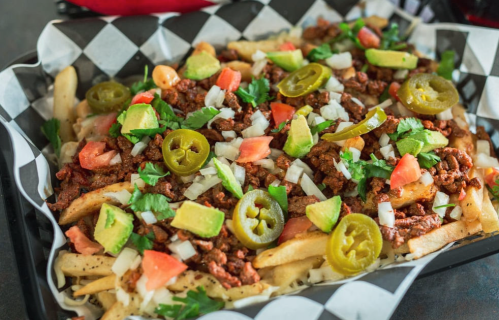 A platter of loaded fries topped with seasoned meat, tomatoes, onions, jalapeños, avocado, and fresh cilantro.