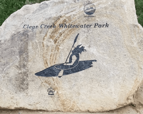 A stone sign for Clear Creek Whitewater Park featuring a kayaker graphic.
