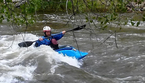 A kayaker in a blue kayak navigates through turbulent whitewater, wearing a helmet and paddling vigorously.