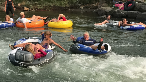 People enjoying a sunny day floating on inner tubes in a river, surrounded by rocks and greenery.