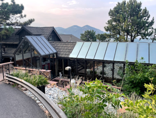 A modern building with glass features, surrounded by greenery and mountains in the background.