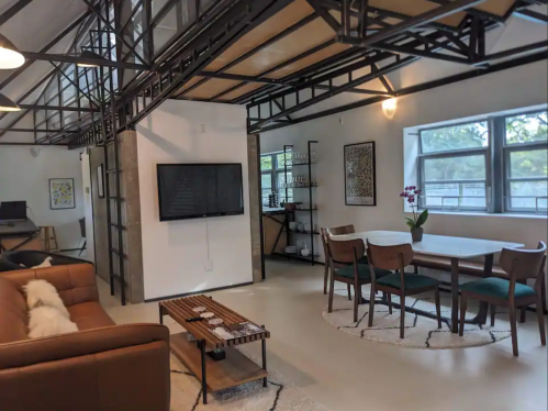 Modern open-concept living space featuring a sofa, dining area, and large windows with natural light.