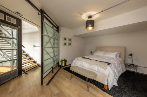 Cozy bedroom with a sliding glass door, wooden stairs, and modern decor, featuring a bed, lamp, and small bench.