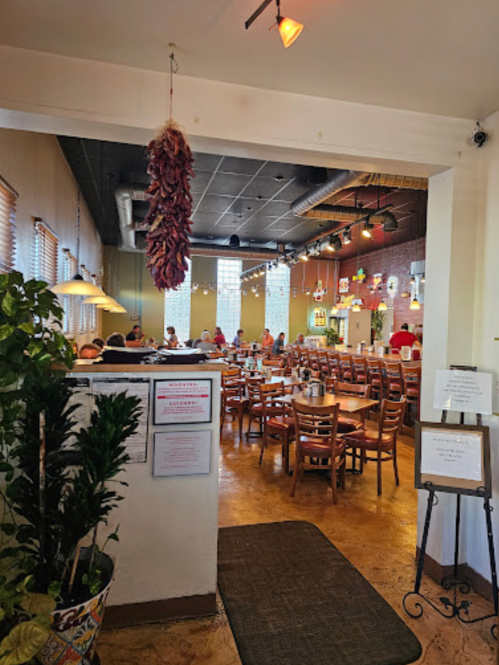 Interior of a restaurant with wooden tables, chairs, and a hanging chili pepper decoration. Bright and inviting atmosphere.