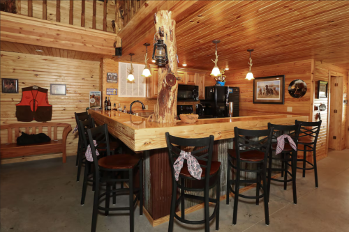 Cozy wooden bar area with high chairs, rustic decor, and a central wooden pillar in a warmly lit space.